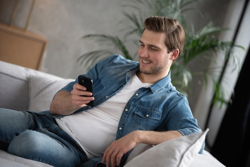 Happy man sitting on a couch and checking his mobile phone