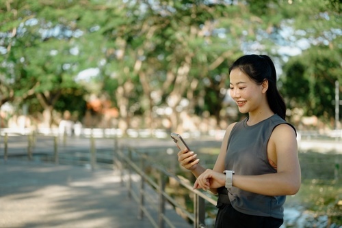Asian woman checking her mobile phone during a running break in the park